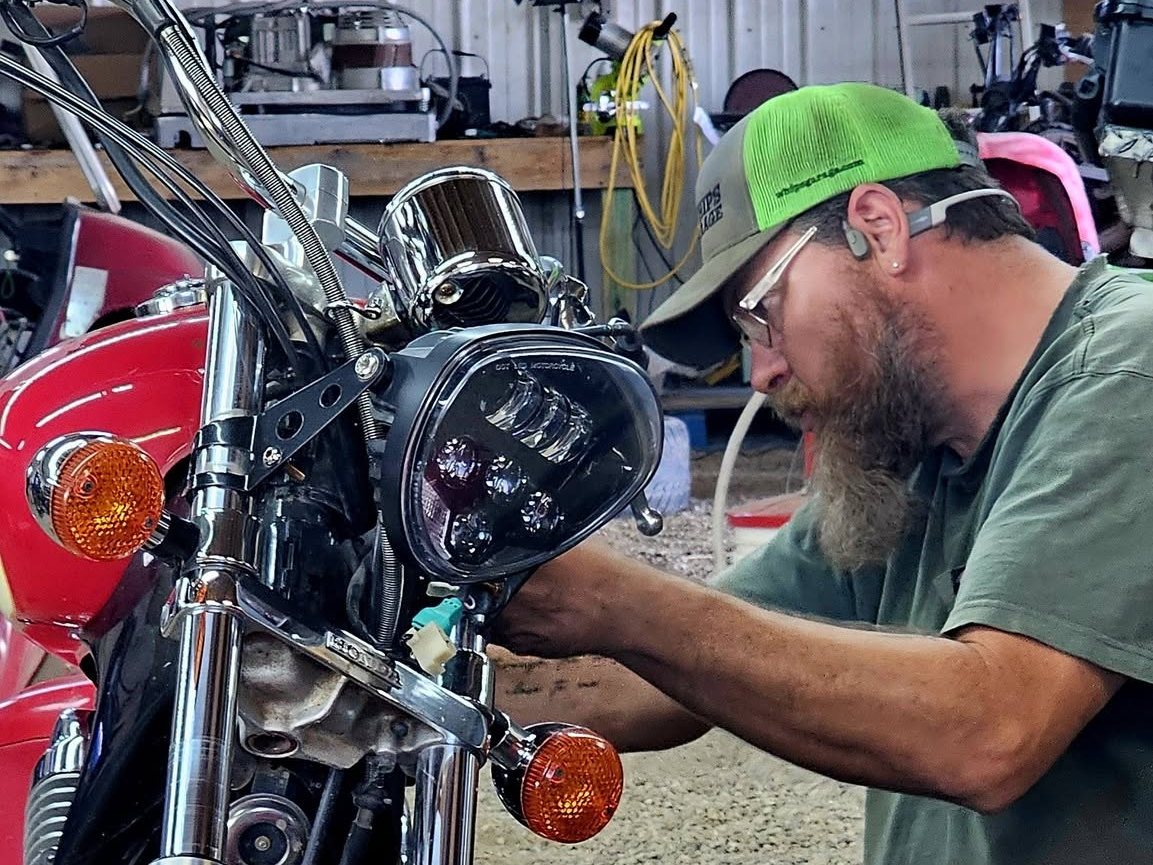 A Whips Garage mechanic working on a motorcycle headlight in the shop